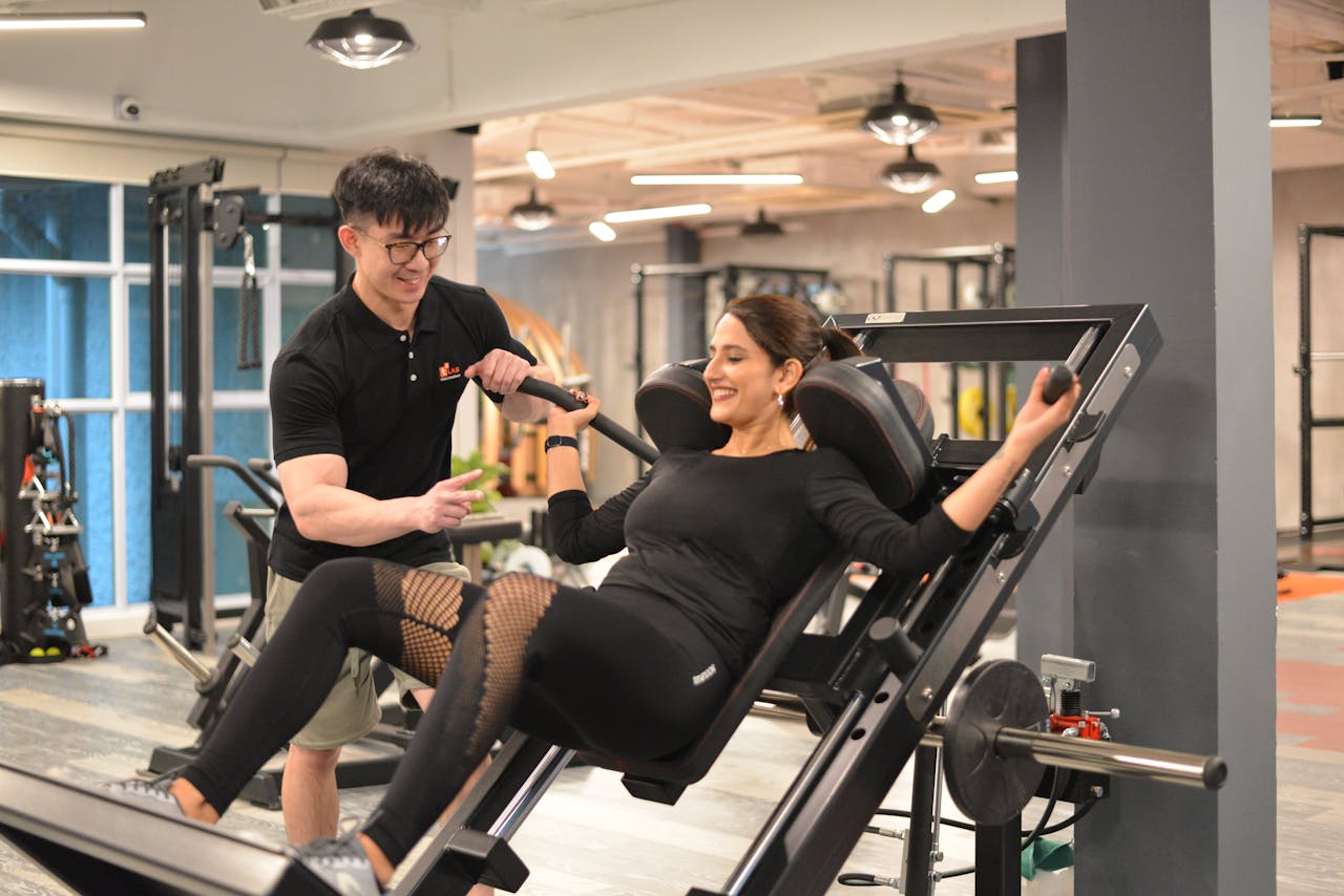 Services A personal trainer helps a woman with leg presses at a modern gym in Singapore.