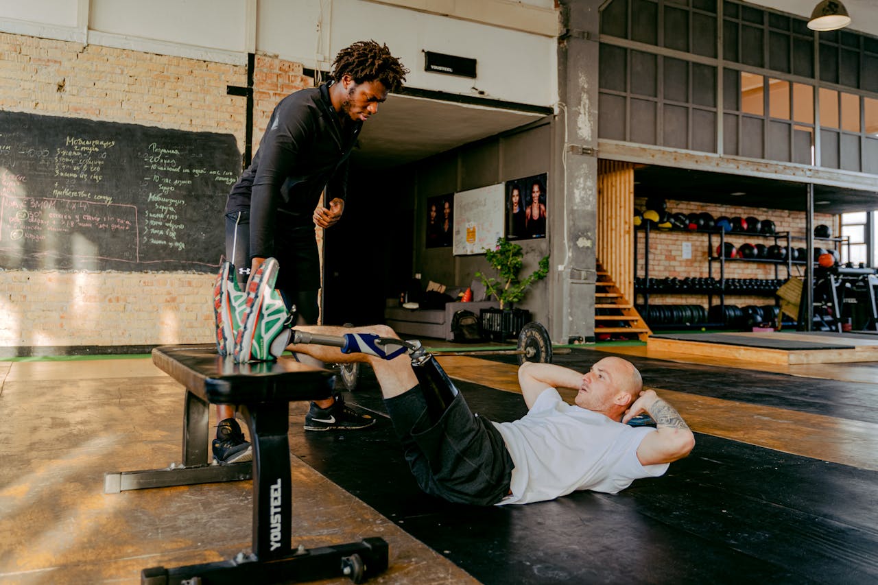 Services Man with prosthetic leg doing crunches in gym with personal trainer's support.