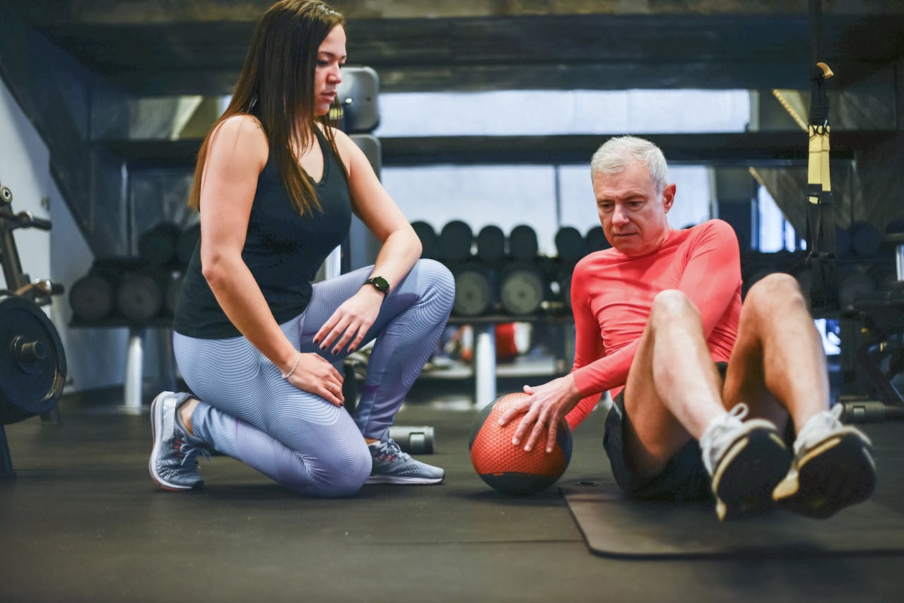 About A senior man exercising with a personal trainer in a gym, focusing on core workouts.