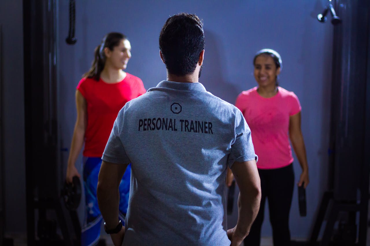 Services Back view of a personal trainer guiding two women during a gym session indoors.